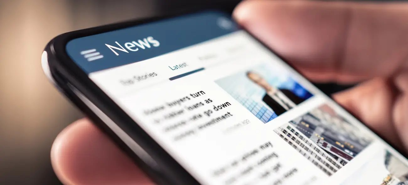 Press & Media A hand holding a smartphone displaying an open news app.